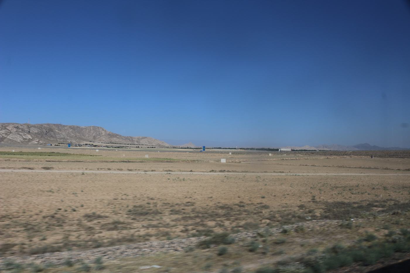 Wide desert landscape with distant mountains under a clear blue sky, seen from a moving train.